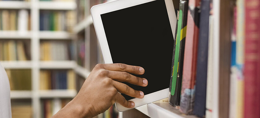 Schmuckbild: Hand nimmt Tablet aus einem Bücherregal