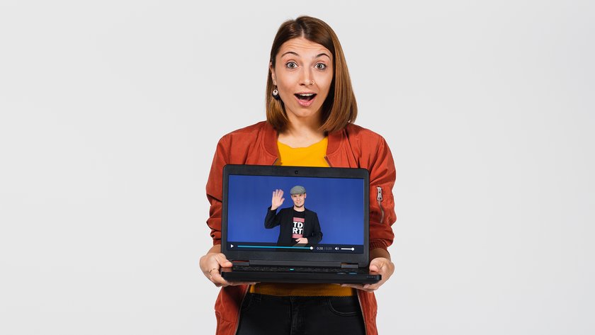 Frau mit begeistertem Gesichtsausdruck hält Laptop, auf dem das Begrüßungsvideo von Studienberater Thomas Bartl zu sehen ist. (öffnet Vergrößerung des Bildes)