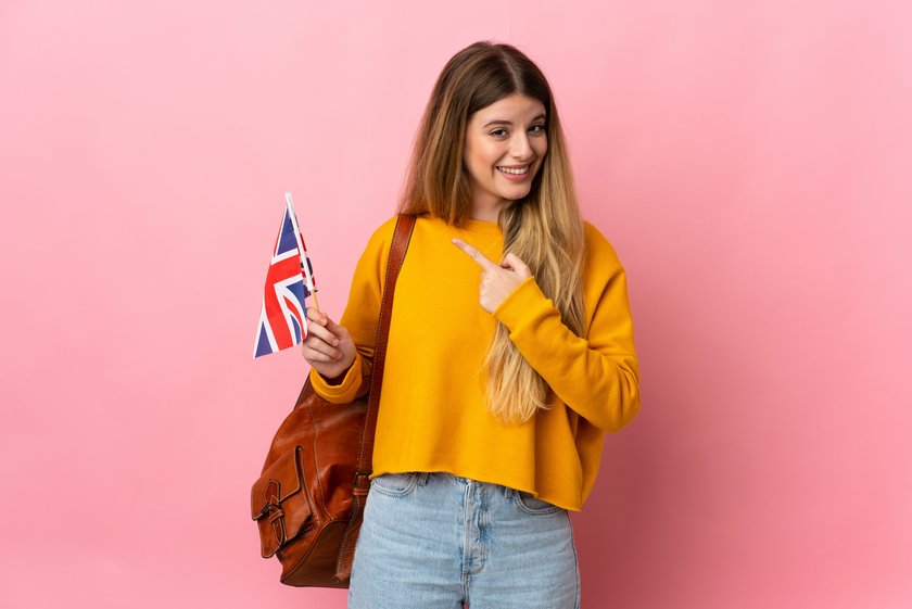 Young blonde woman holding an United Kingdom flag isolated on white background pointing to the side to present a product