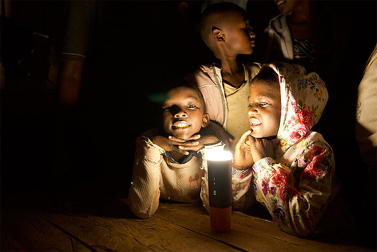Kinder sitzen um am Tisch mit einer Mango Solar Lampe und lernen zusammen (öffnet Vergrößerung des Bildes)